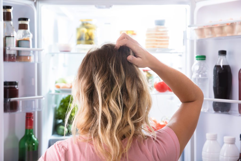 Woman confused about what to eat in front of fridge